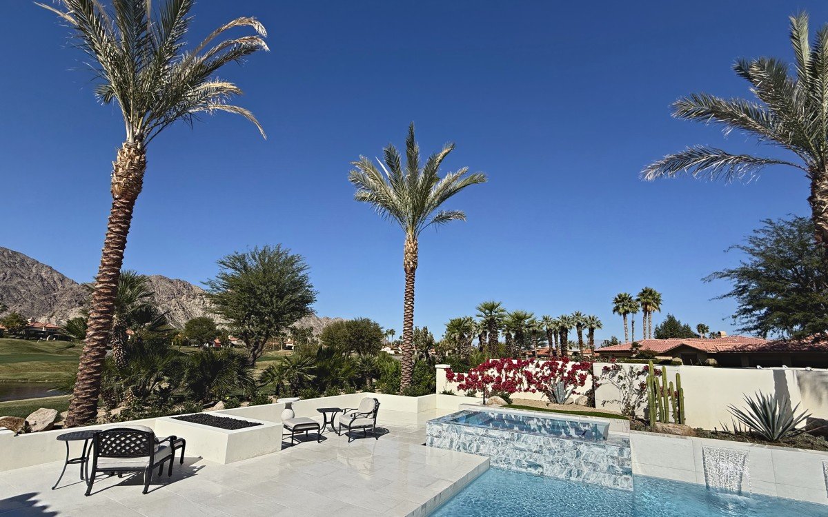 Finished backyard with tall palms, a fire table, spa and patio furniture, mountains behind