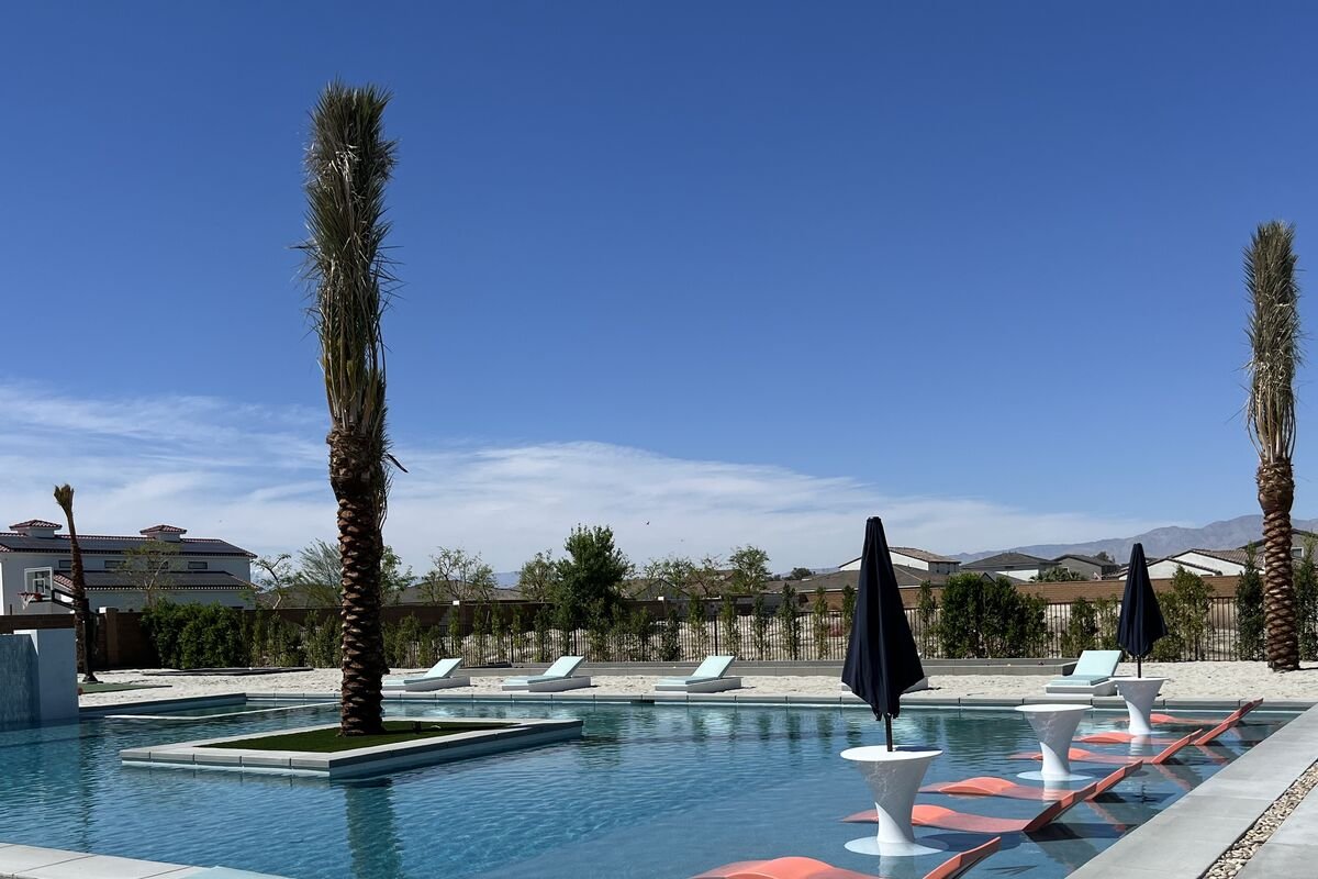 Date palm on a turf island in the middle of a resort-style pool, with a second palm and desert mountains beyond