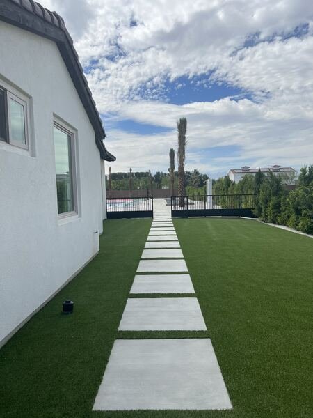 Concrete pads set in artificial turf along the side of a modern home