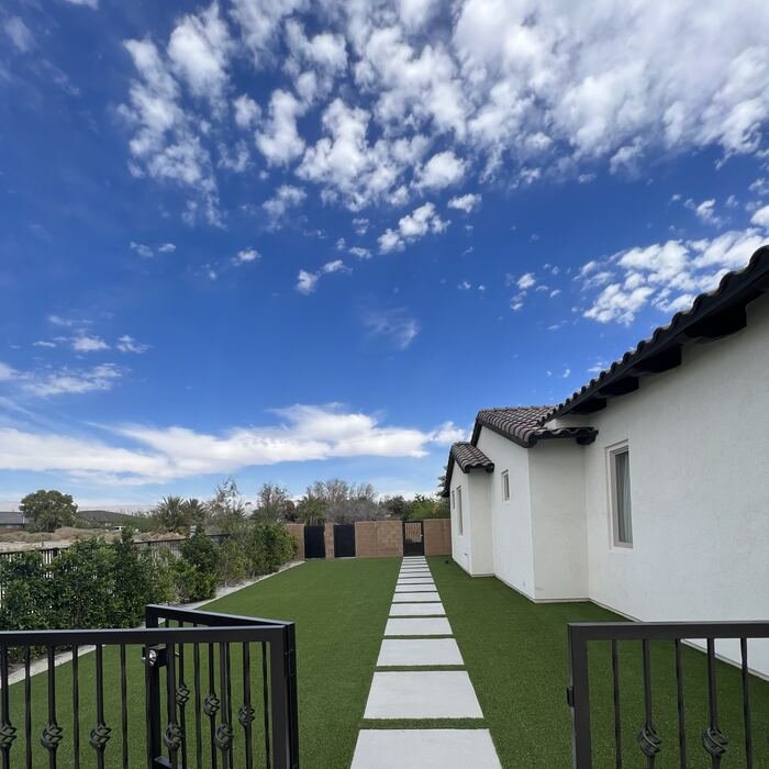 Concrete stepping-stone walkway through artificial turf leading to a black gate
