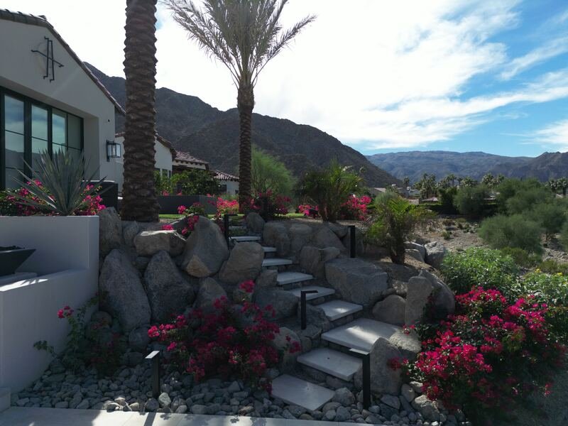 Stone steps climbing through boulders and magenta bougainvillea beside a modern home