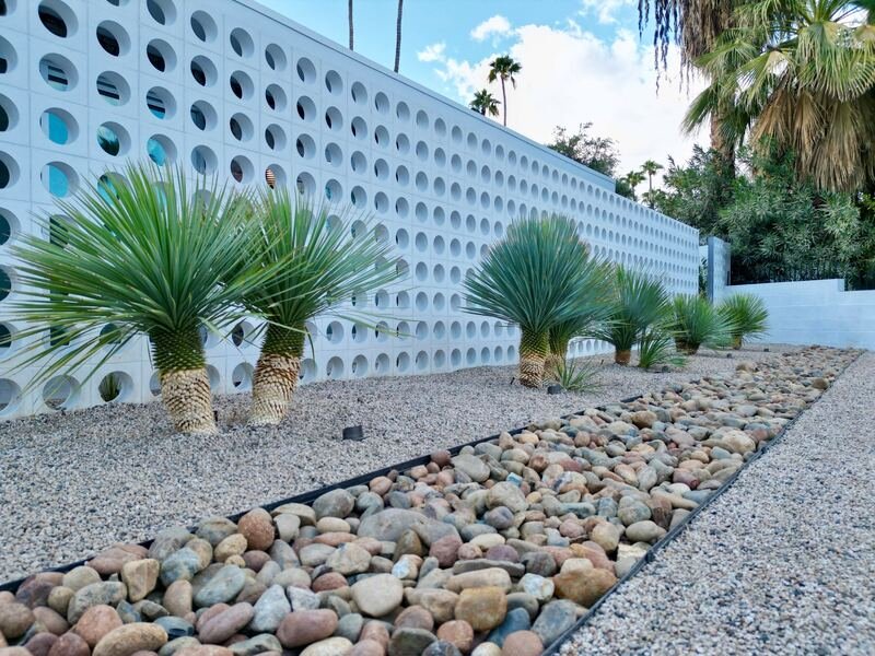 Blue yuccas and agaves above a river-rock dry creek bed in front of a circular breeze-block wall